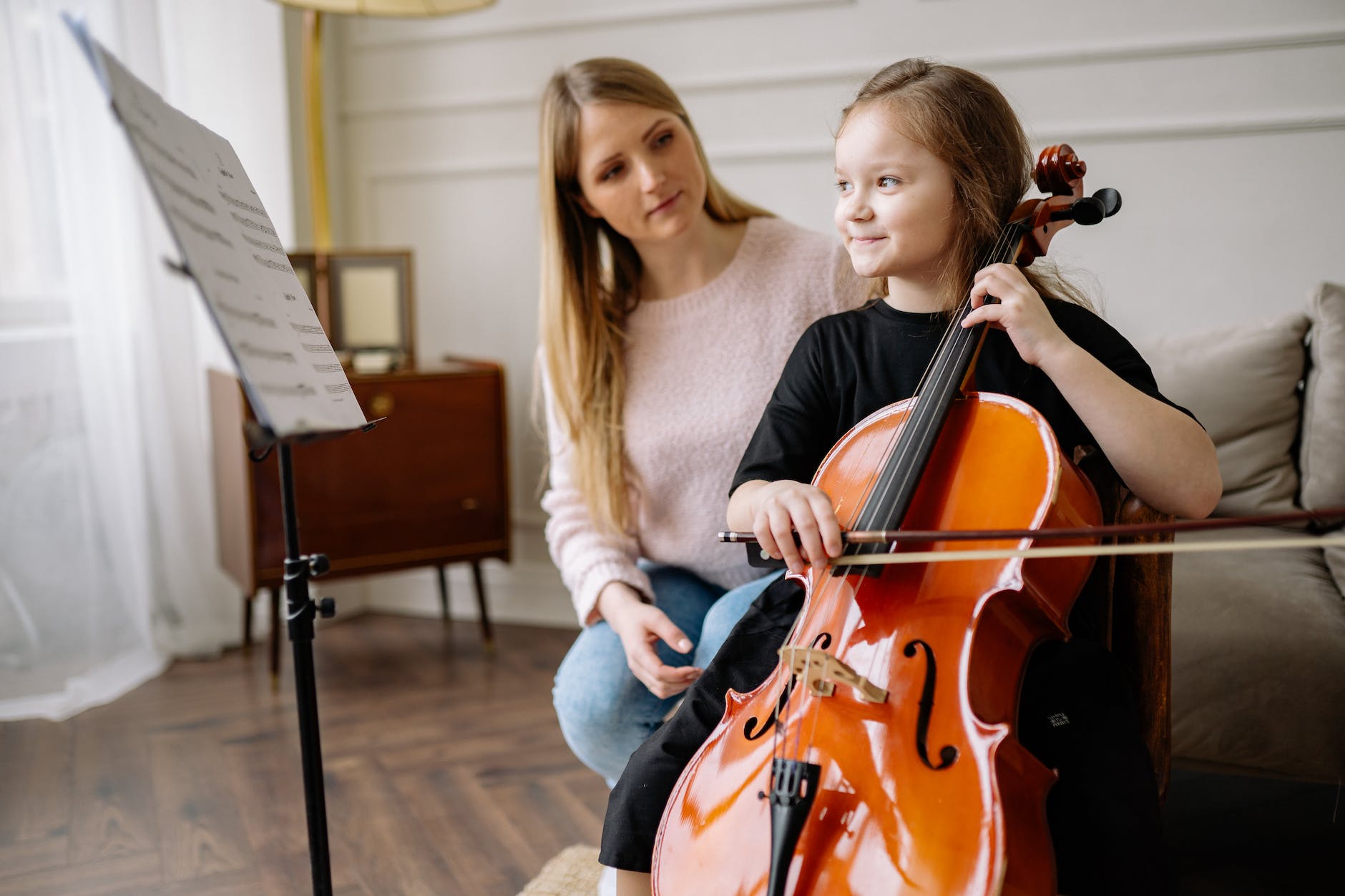girl playing cello beside a woman in pink sweater