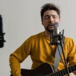 photo of a man in a yellow sweater singing while his eyes are closed
