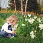 girl sitting on grass smelling white petaled flower