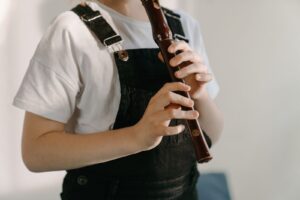 A young musician in casual attire practicing playing a flute indoors, focusing on learning.