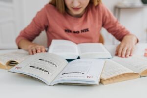 A woman in pink long sleeves studying multiple open books indoors.