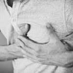 Black and white photo of a man clutching his chest, indicating discomfort or pain.